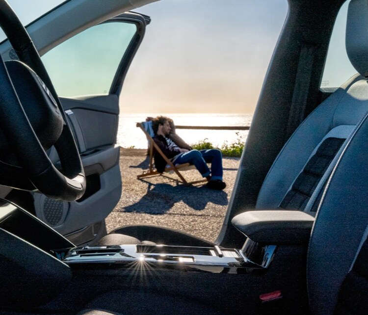 Чоловік сидить на березі моря у складаному кріслі біля Citroën C4, вигляд крізь передній ряд сидінь